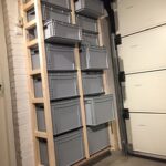 Wooden wall-mounted shelving unit holding grey plastic storage bins in a basement garage.