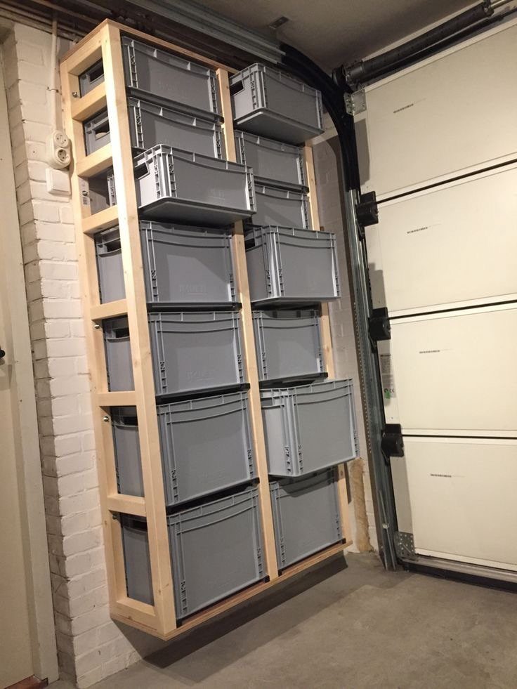 Wooden wall-mounted shelving unit holding grey plastic storage bins in a basement garage.