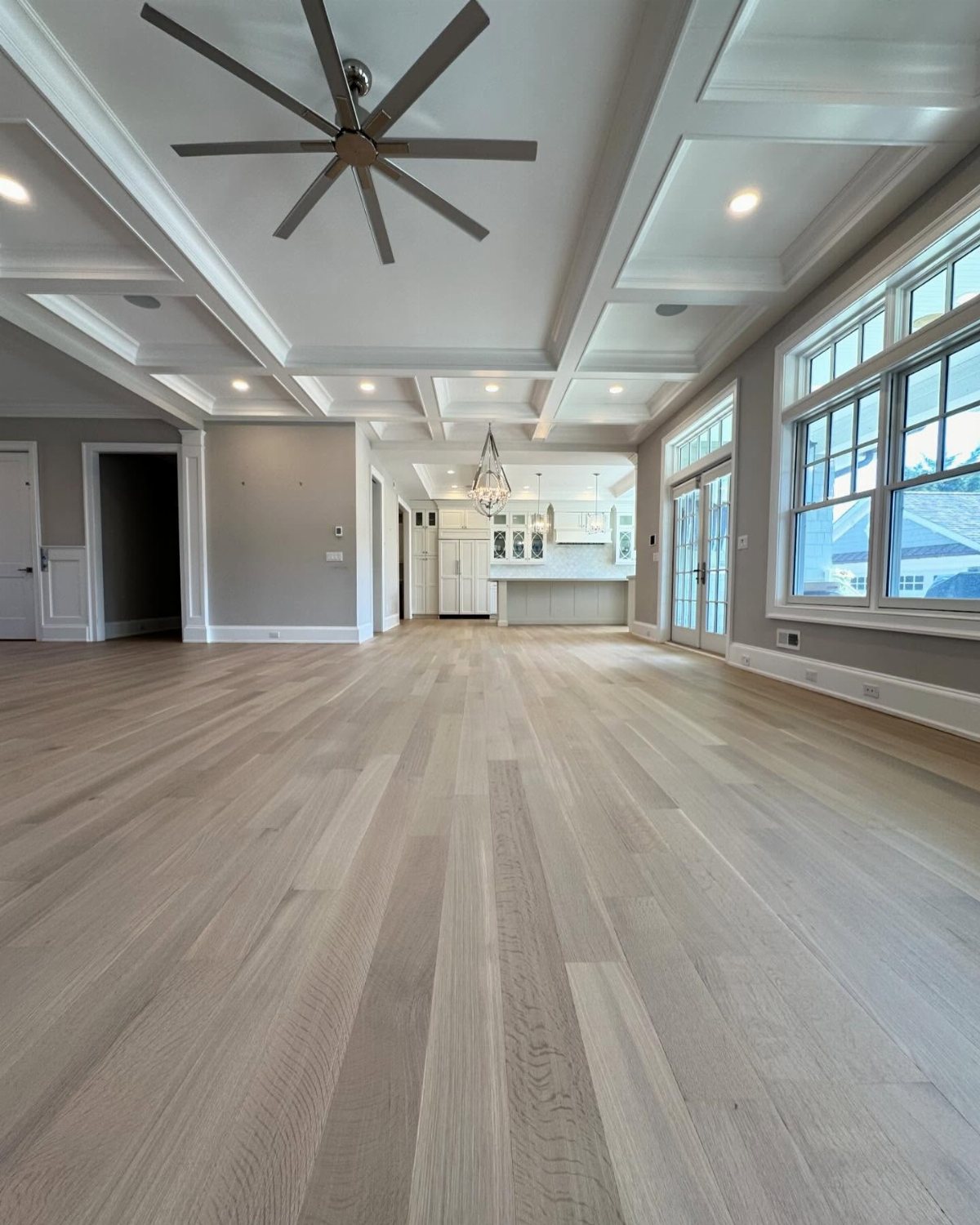 Light wood plank flooring in a bright, open-concept room with white coffered ceilings.