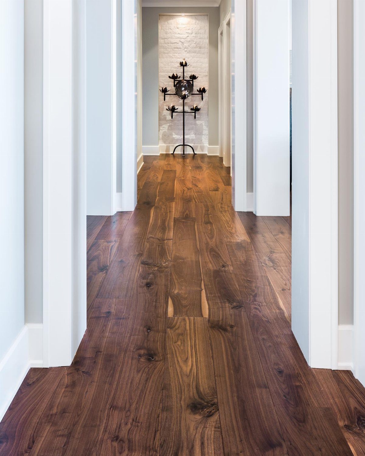 Dark walnut wood plank flooring stretching through a bright white hallway toward a decorative stand.