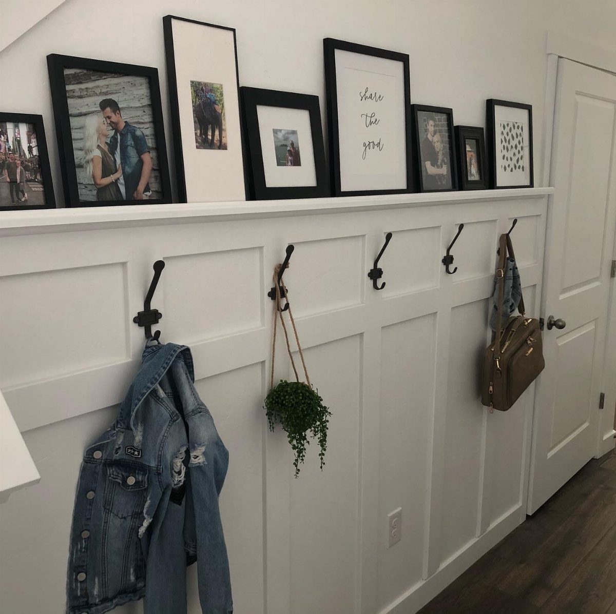 White board and batten wall with a shelf holding framed pictures and hooks with items hanging.