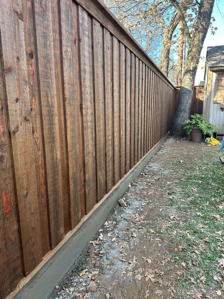 A tall, dark brown stained wooden privacy fence running along a yard next to a tree.