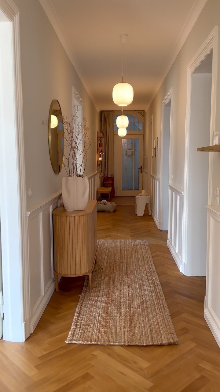 A bright hallway featuring white wainscoting and a chair rail against light blue walls.