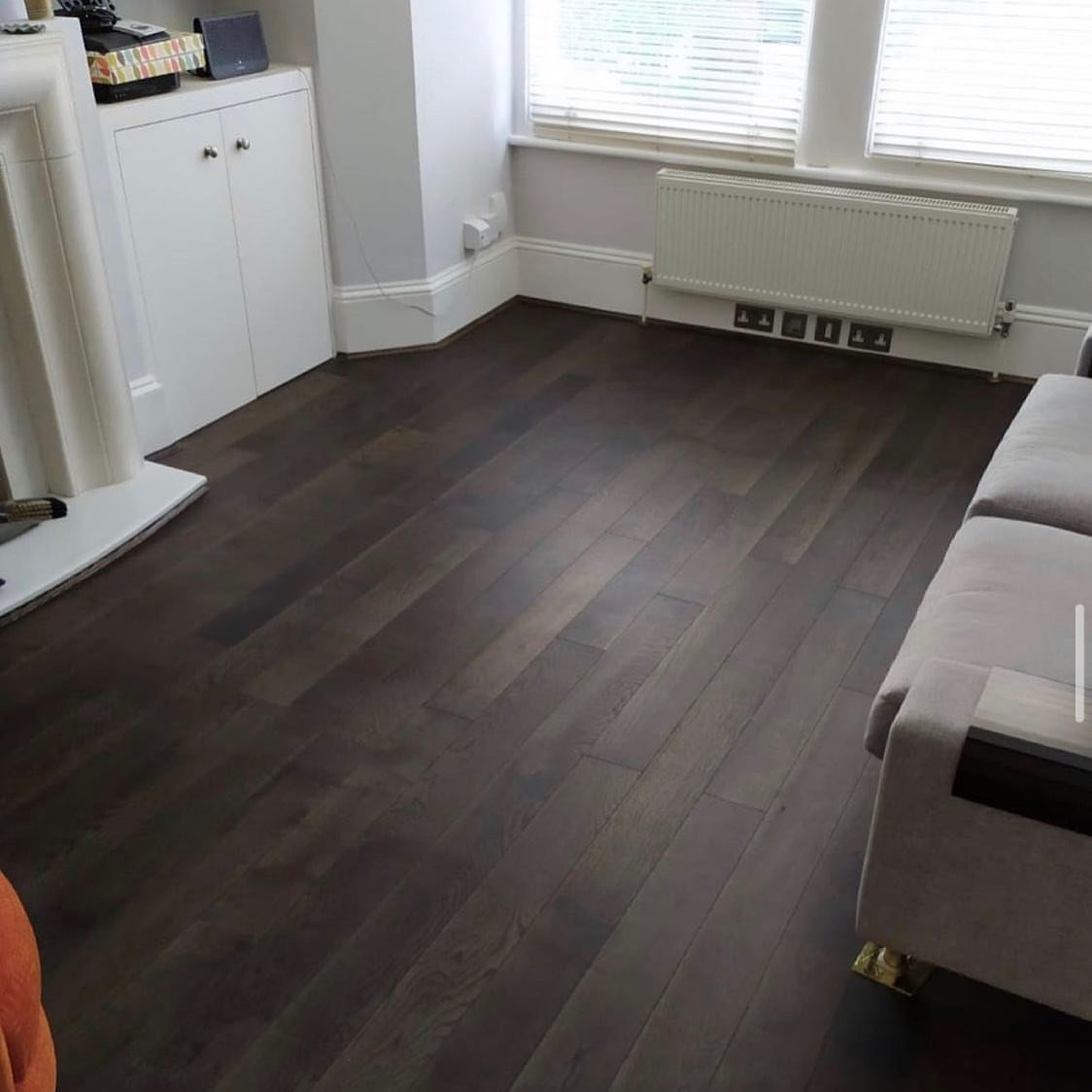 Dark chocolate brown hardwood floor planks in a bright living room with white walls.