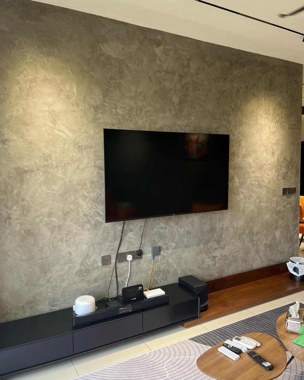 A black television mounted on a textured grey concrete-style accent wall above a media console.