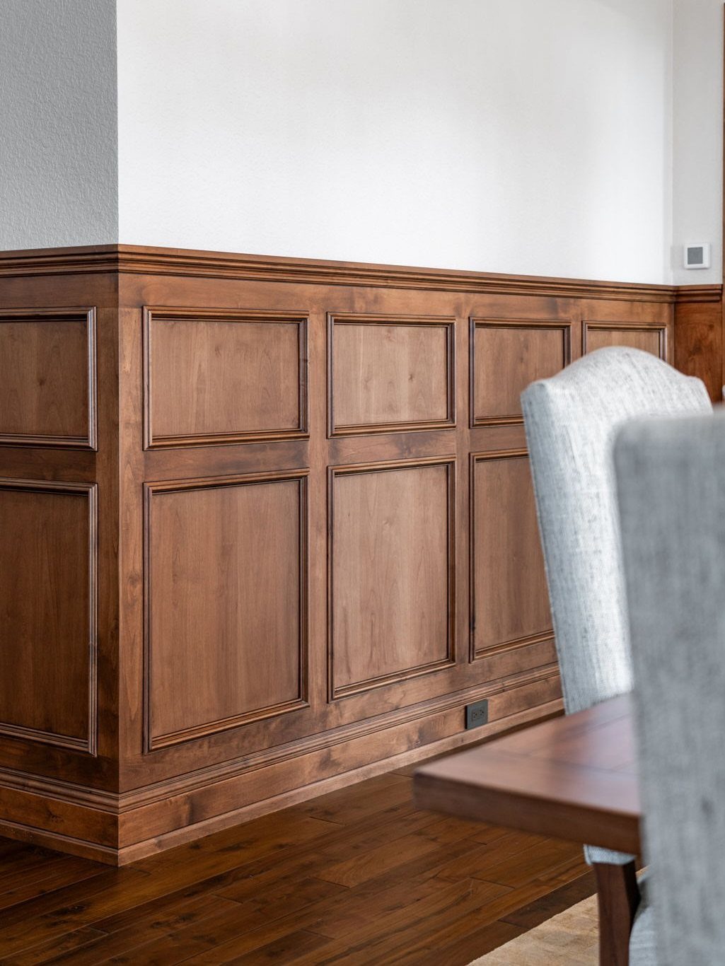 Dark wood raised panel wainscoting installed on a dining room wall near a wooden table.