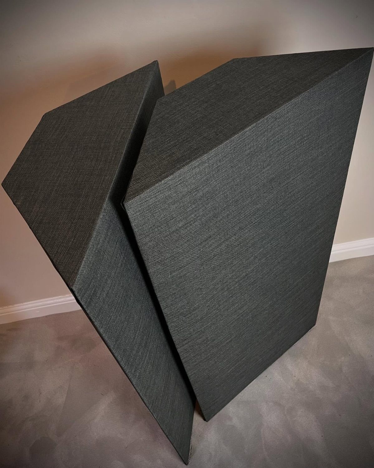 Two dark grey fabric-wrapped acoustic panels leaning against a wall in a corner.