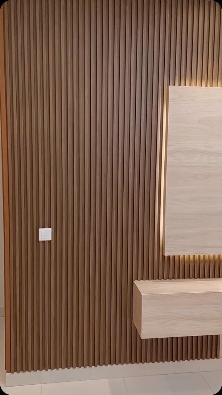 Vertical fluted wood paneling on a wall with floating wooden shelves and backlight.