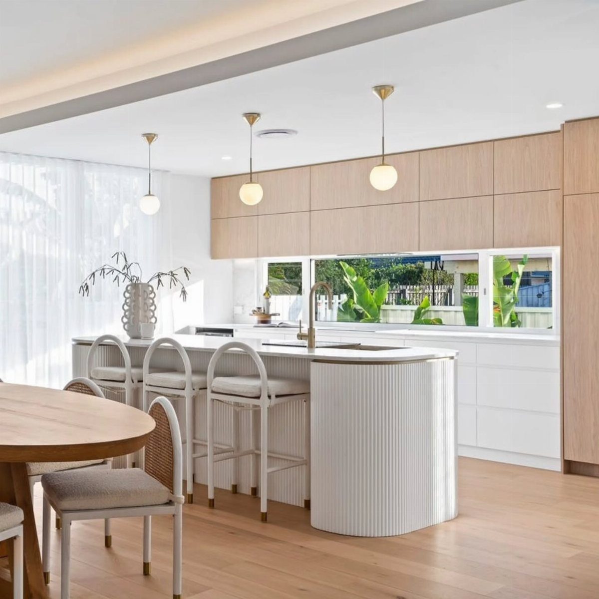 Modern kitchen with white island, light wood cabinets, and light oak wood flooring.