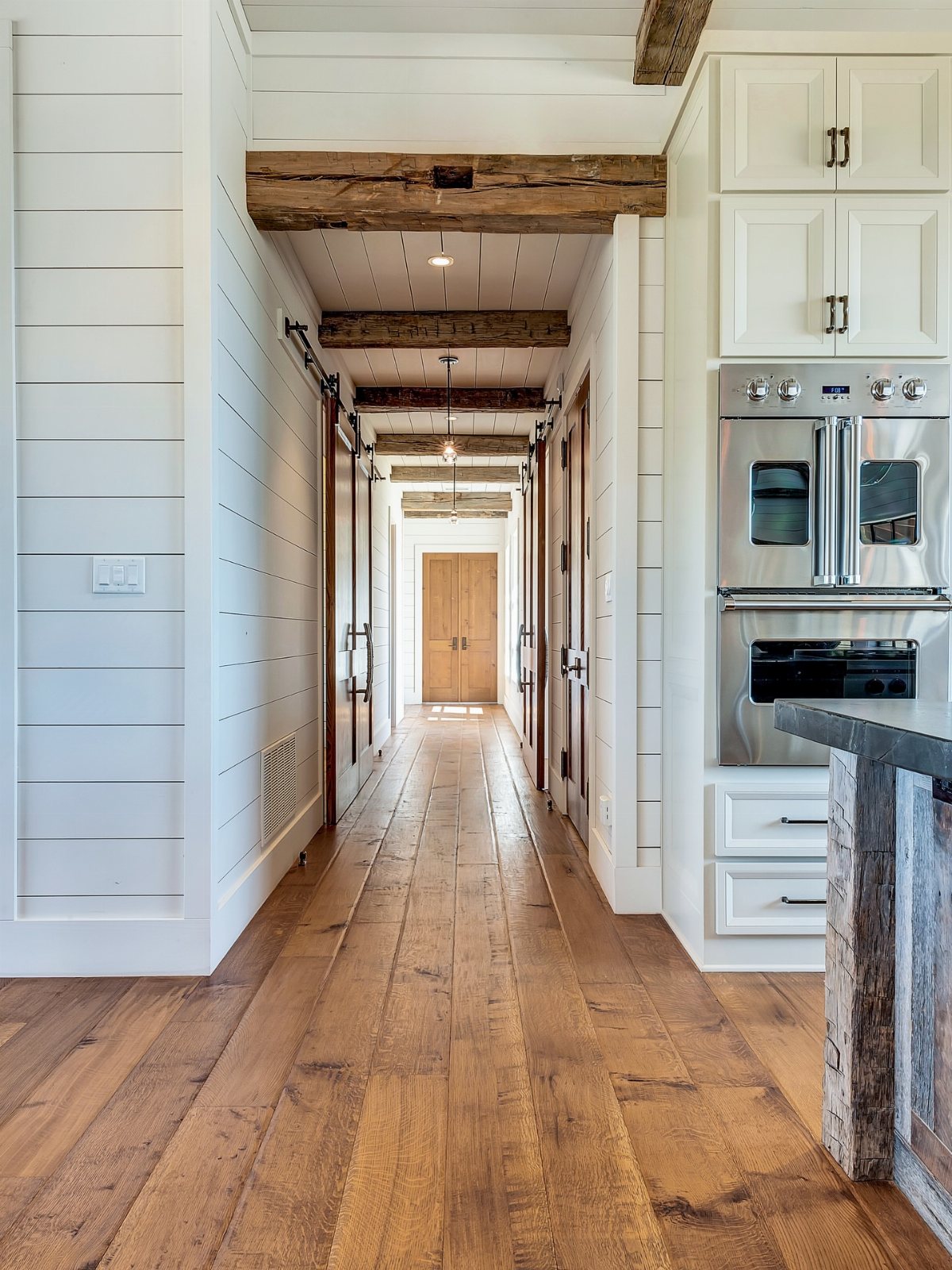 Wide light-brown wooden planks running through a bright hallway with white shiplap walls.