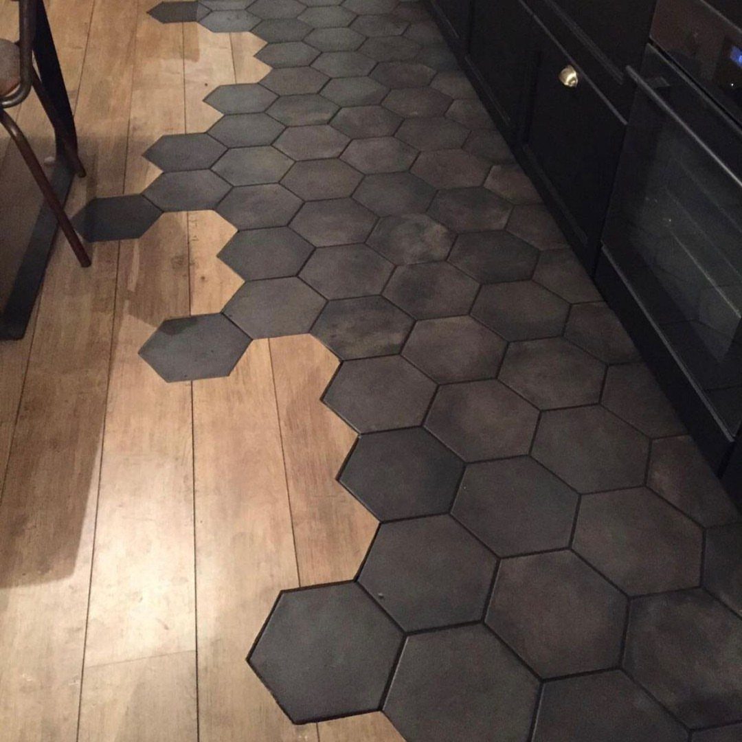 Dark grey hexagonal tiles transitioning into a light wood plank floor in a kitchen.