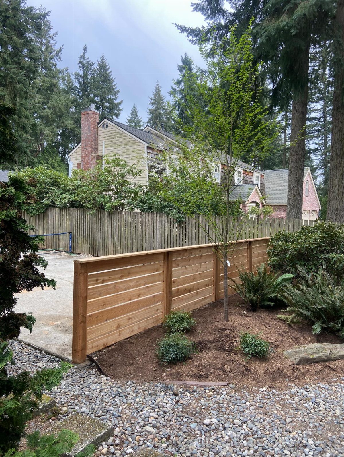 Horizontal wood fence installed in a landscaped garden with mulch, small plants, and a house in the background.