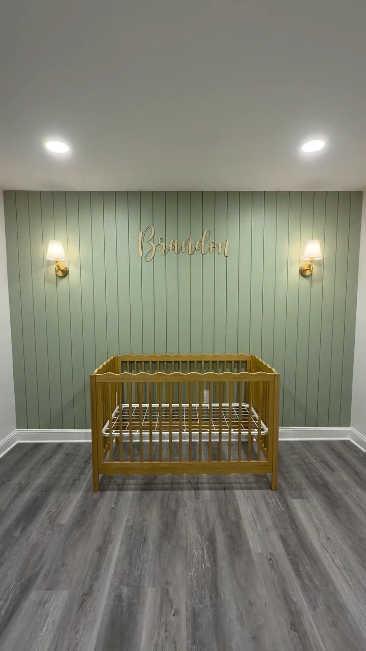 Sage green board and batten wall with a wooden crib and gold name sign.