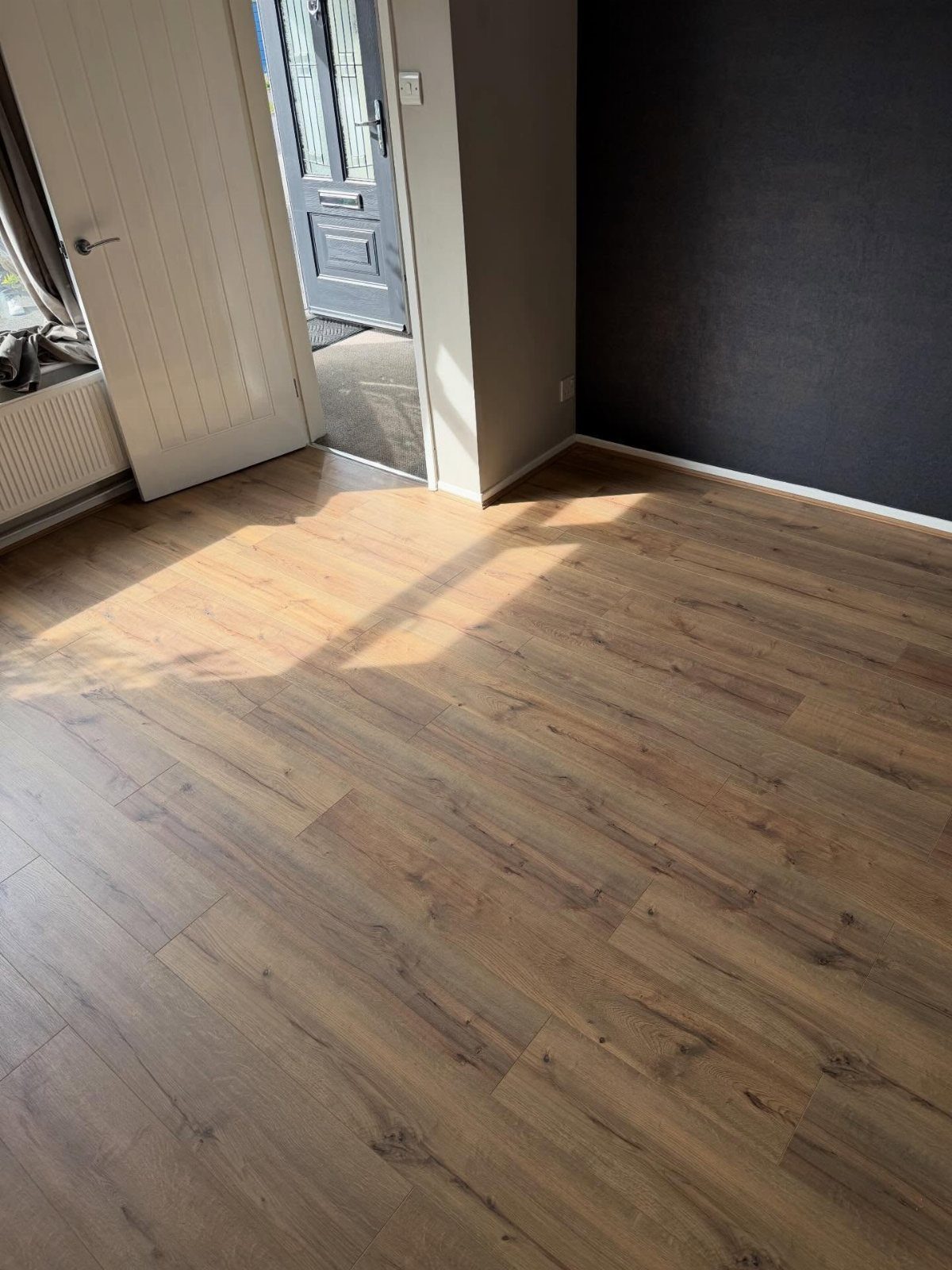 Light brown wood-effect laminate flooring planks in a sunlit room with an open white door.