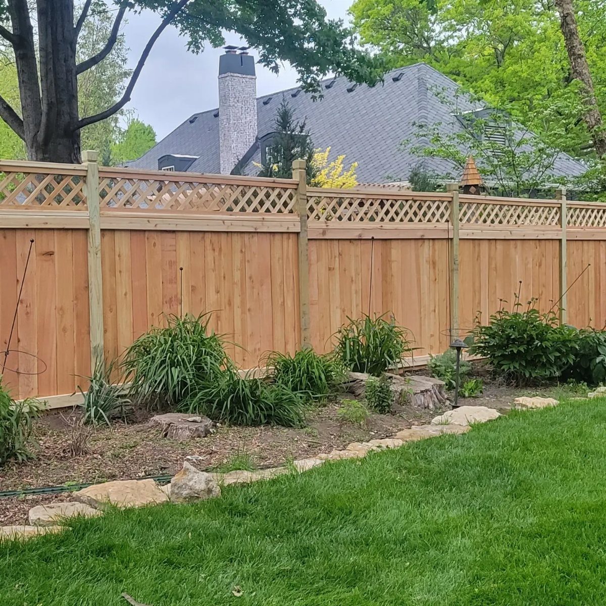 A wooden privacy fence with a decorative lattice top panel bordering a garden.