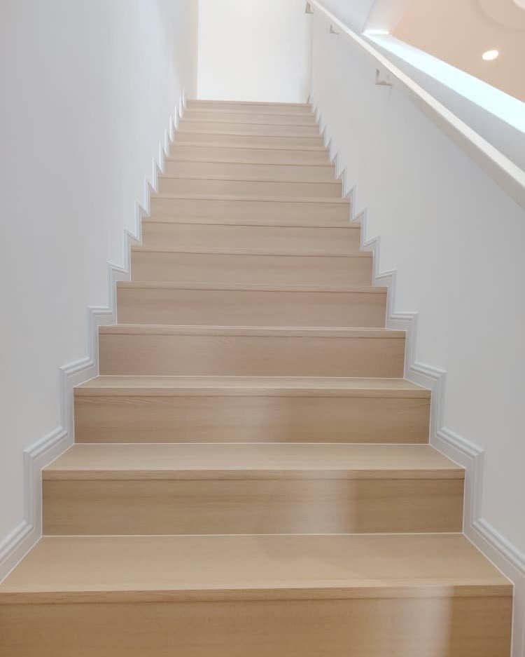 Light-colored wooden stairs leading up between two white walls in a bright interior.