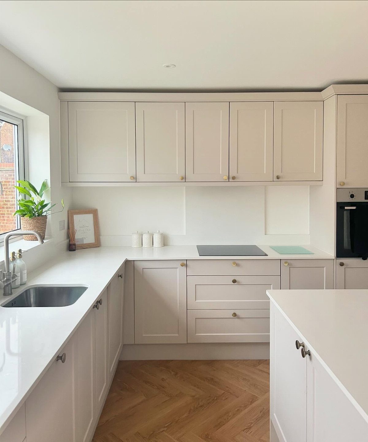White shaker kitchen cabinets with white countertops and a light oak herringbone wood floor.
