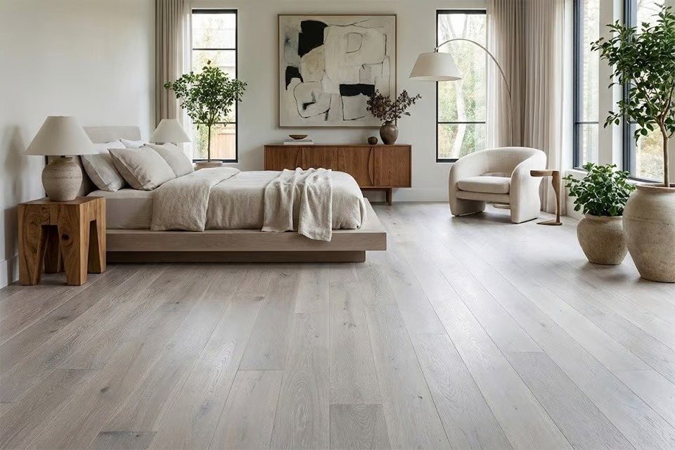 Light gray matte wood flooring in a modern, minimalist bedroom with neutral furniture and large windows.