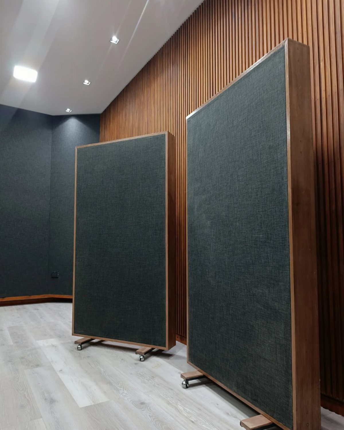 Two large dark grey acoustic panels with wooden frames on wheels in a room.