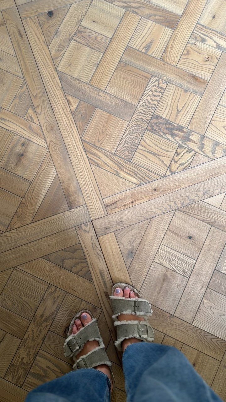 Complex geometric parquet wood flooring with various plank widths and patterns in light brown tones.