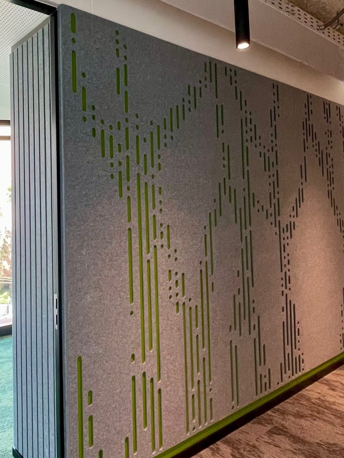 Grey acoustic wall panel featuring a decorative pattern of vertical green slits in a modern room.