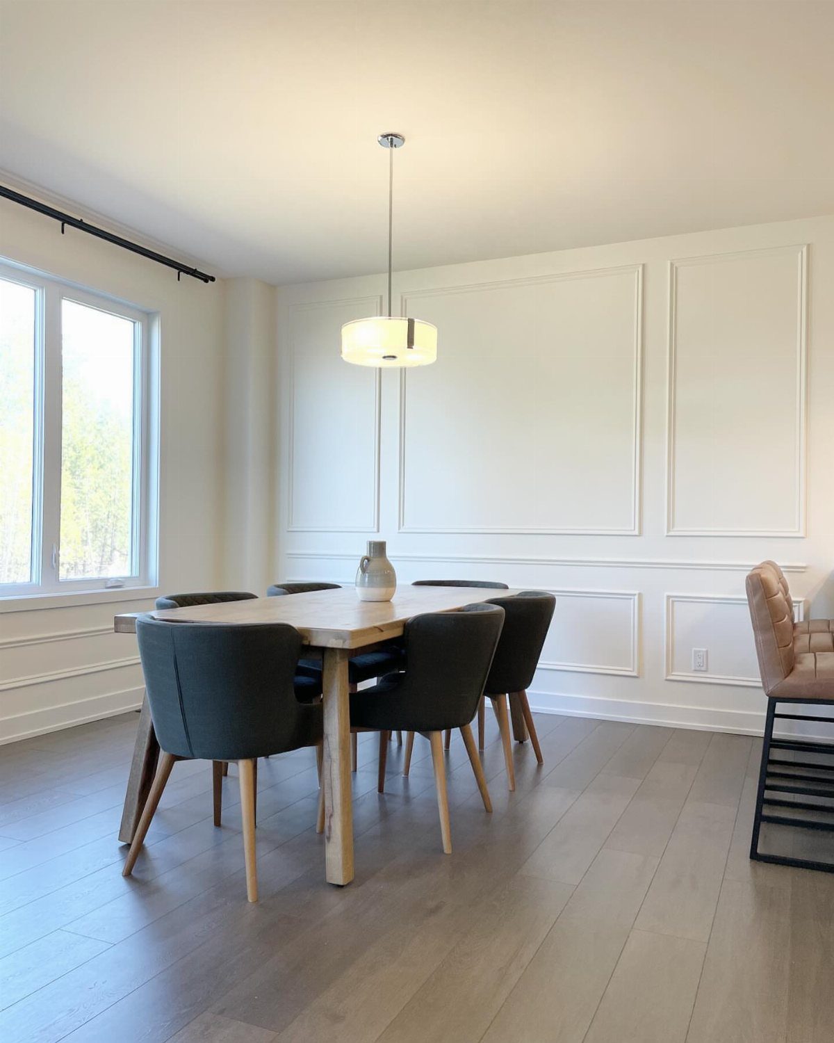Dining room with white picture frame wainscoting, a light wood table, and dark grey chairs.