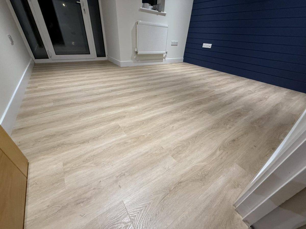 Light wood-effect laminate flooring planks installed in a room with a blue paneled wall.