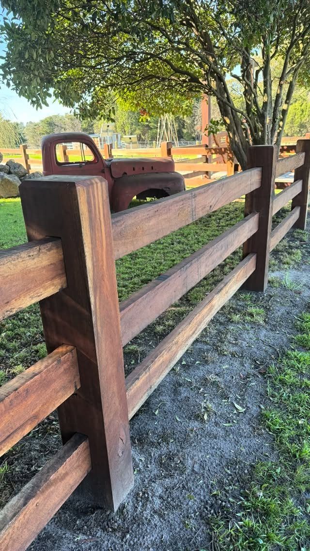 A reddish-brown wooden post and rail fence running through a green grassy yard.