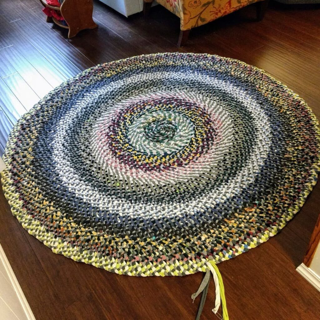 Circular braided rag rug with multicolored fabric strips on a dark wood floor.