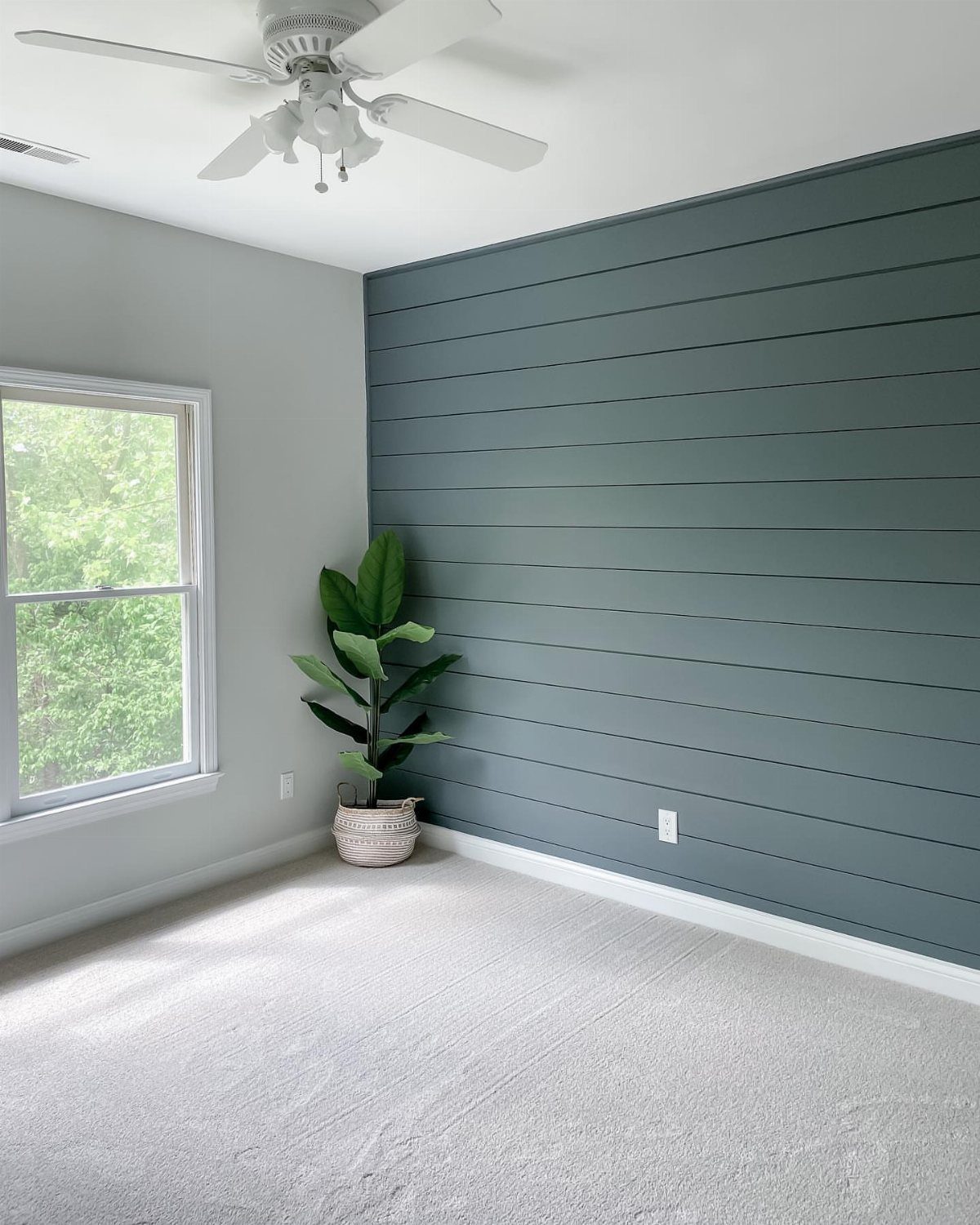Dark teal shiplap accent wall in a room with light gray walls and a white window.