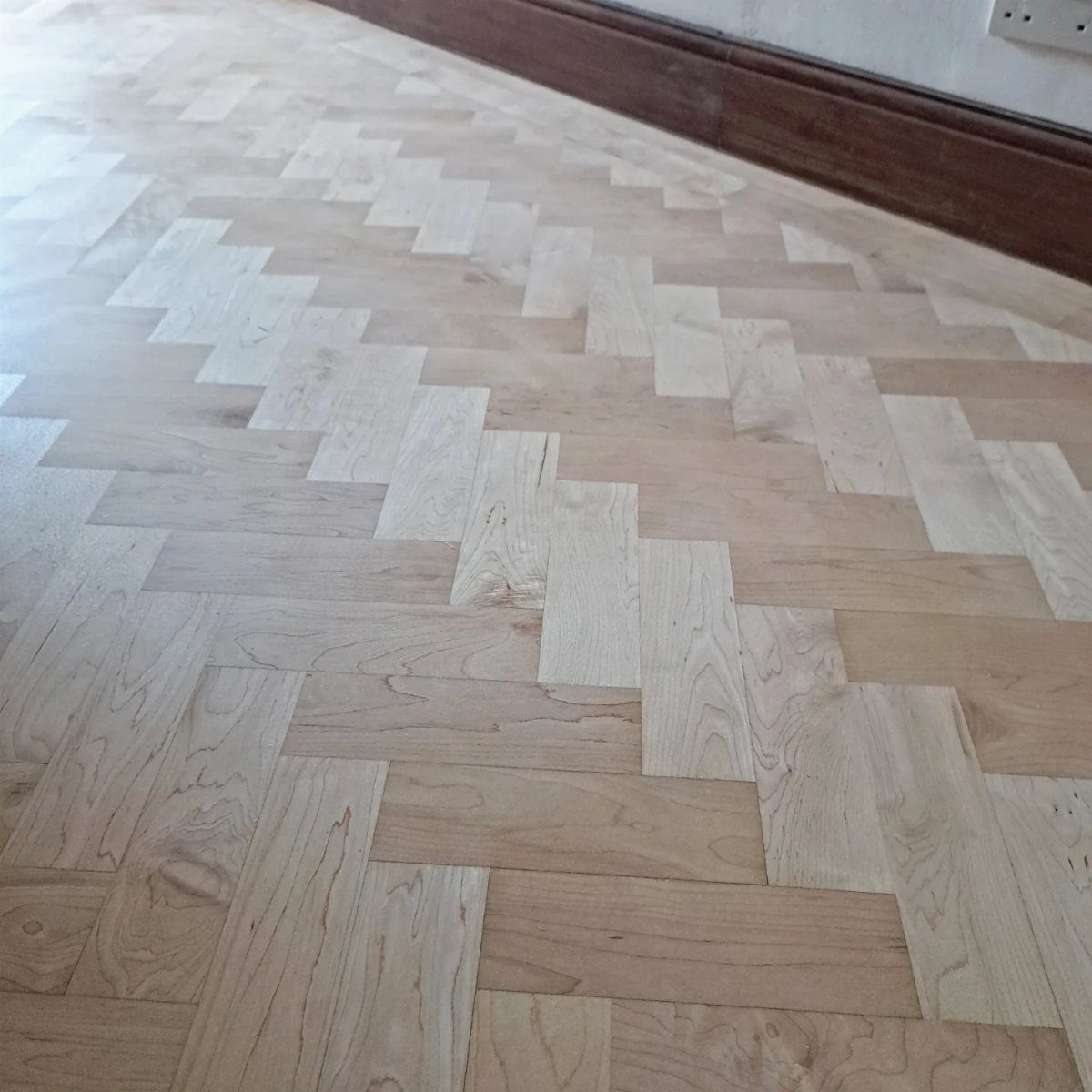 Light maple wood flooring planks arranged in a herringbone pattern with a smooth finish.