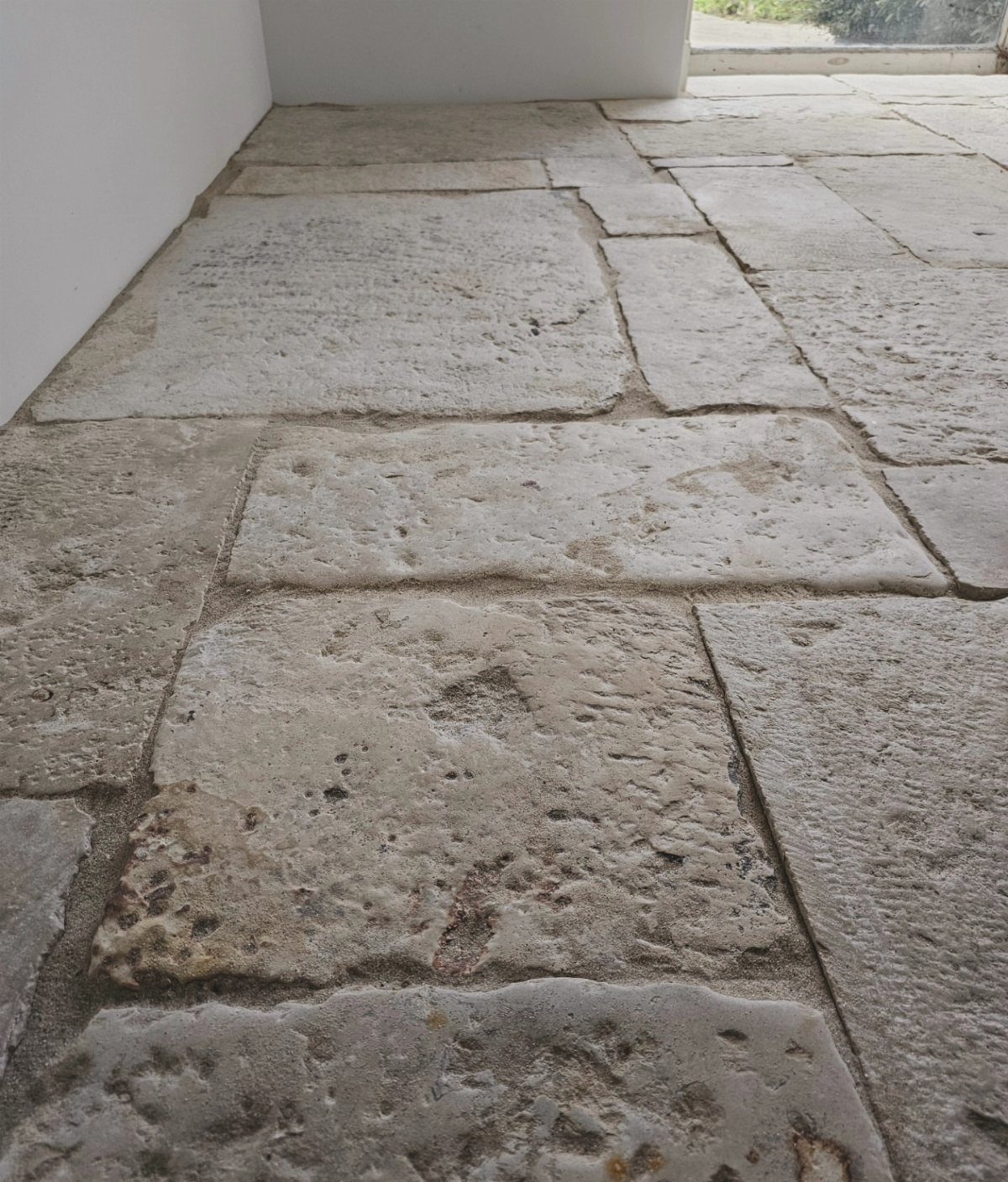 Large, textured light beige stone tiles laid in an irregular pattern on a floor.