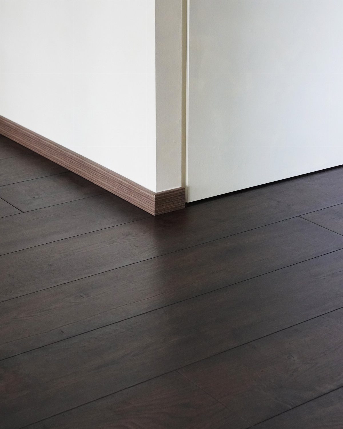 Dark Brown Wood Colors: 13 Ideas for Your Home 12 Dark brown wood flooring planks meeting a white wall with a matching wood baseboard.