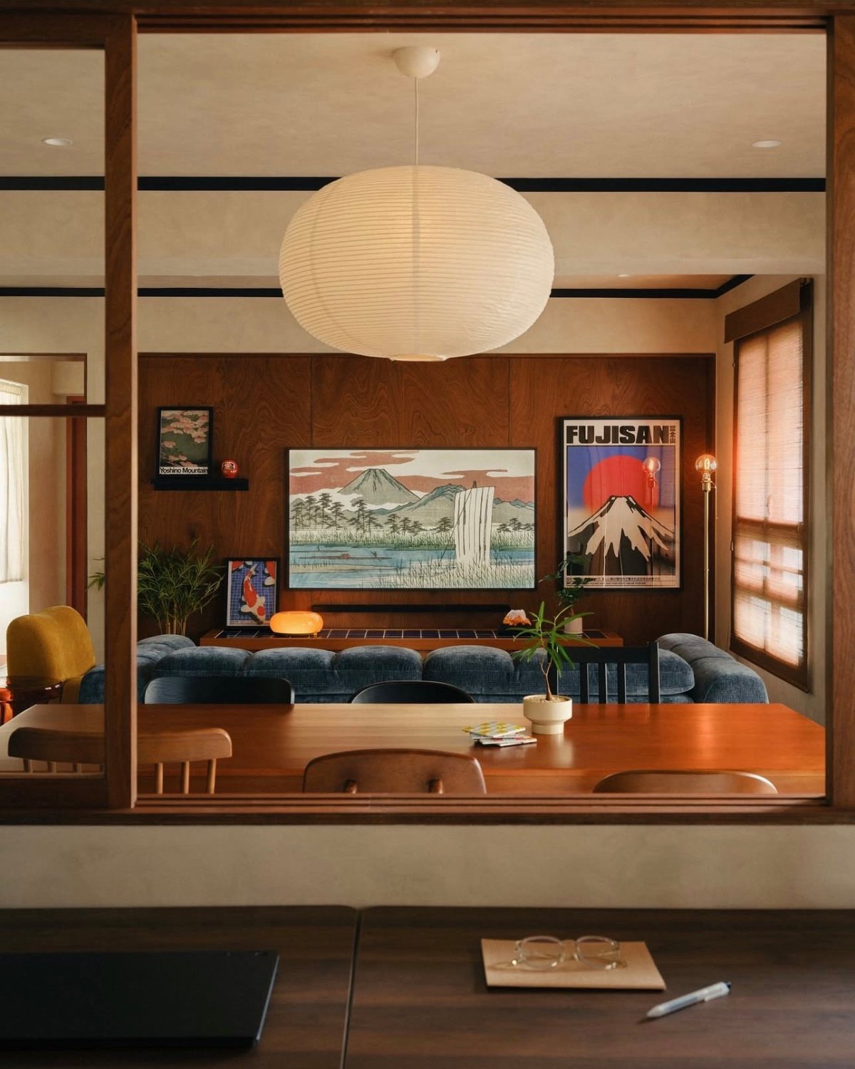 Walnut wood paneling on a living room wall decorated with landscape art and a paper lamp.