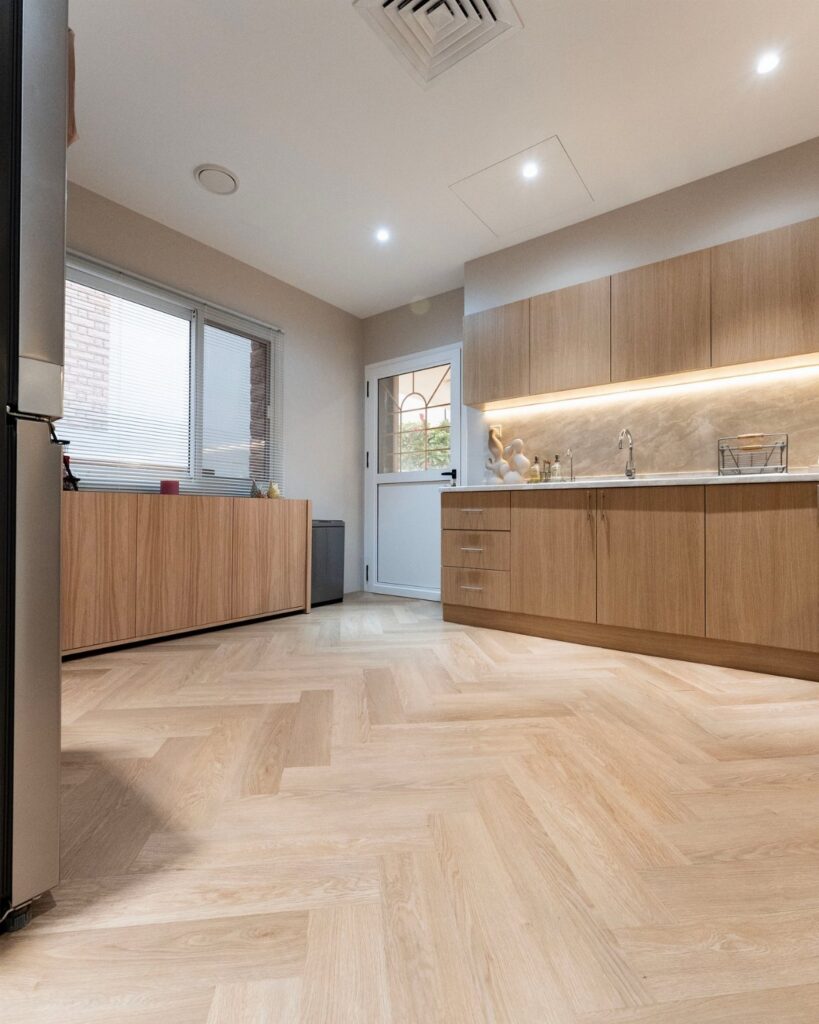 Light oak cabinets and herringbone pattern vinyl flooring in a modern, bright kitchen setting.