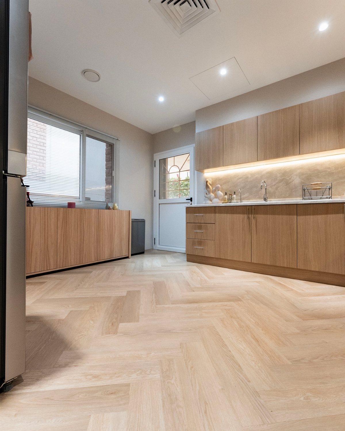 Light oak cabinets and herringbone pattern vinyl flooring in a modern, bright kitchen setting.