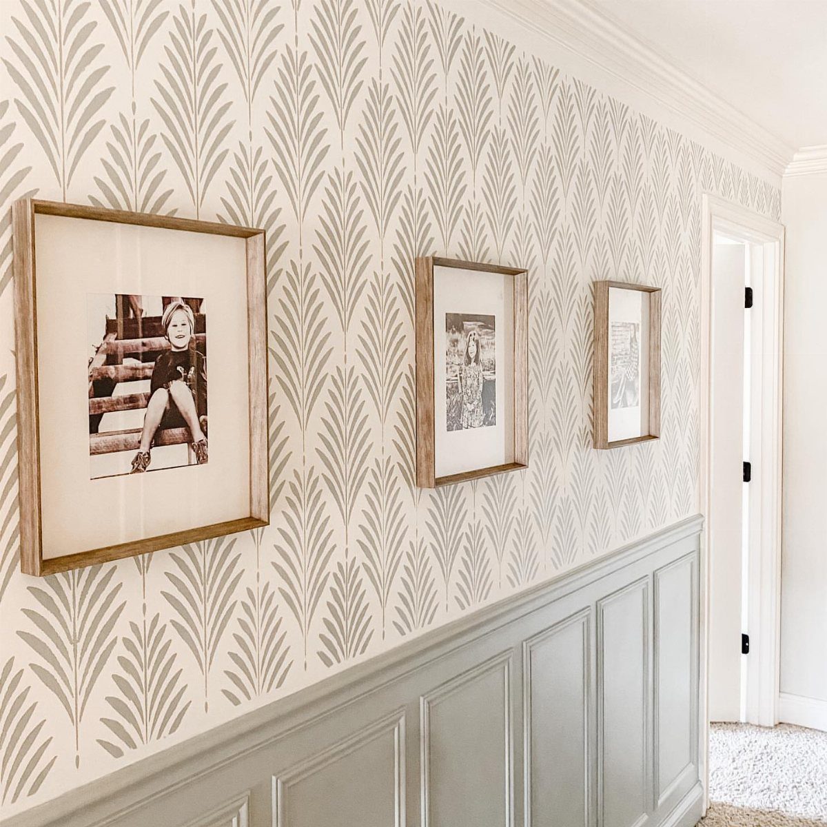 Three framed black and white photos hanging on patterned wallpaper above gray wainscoting.