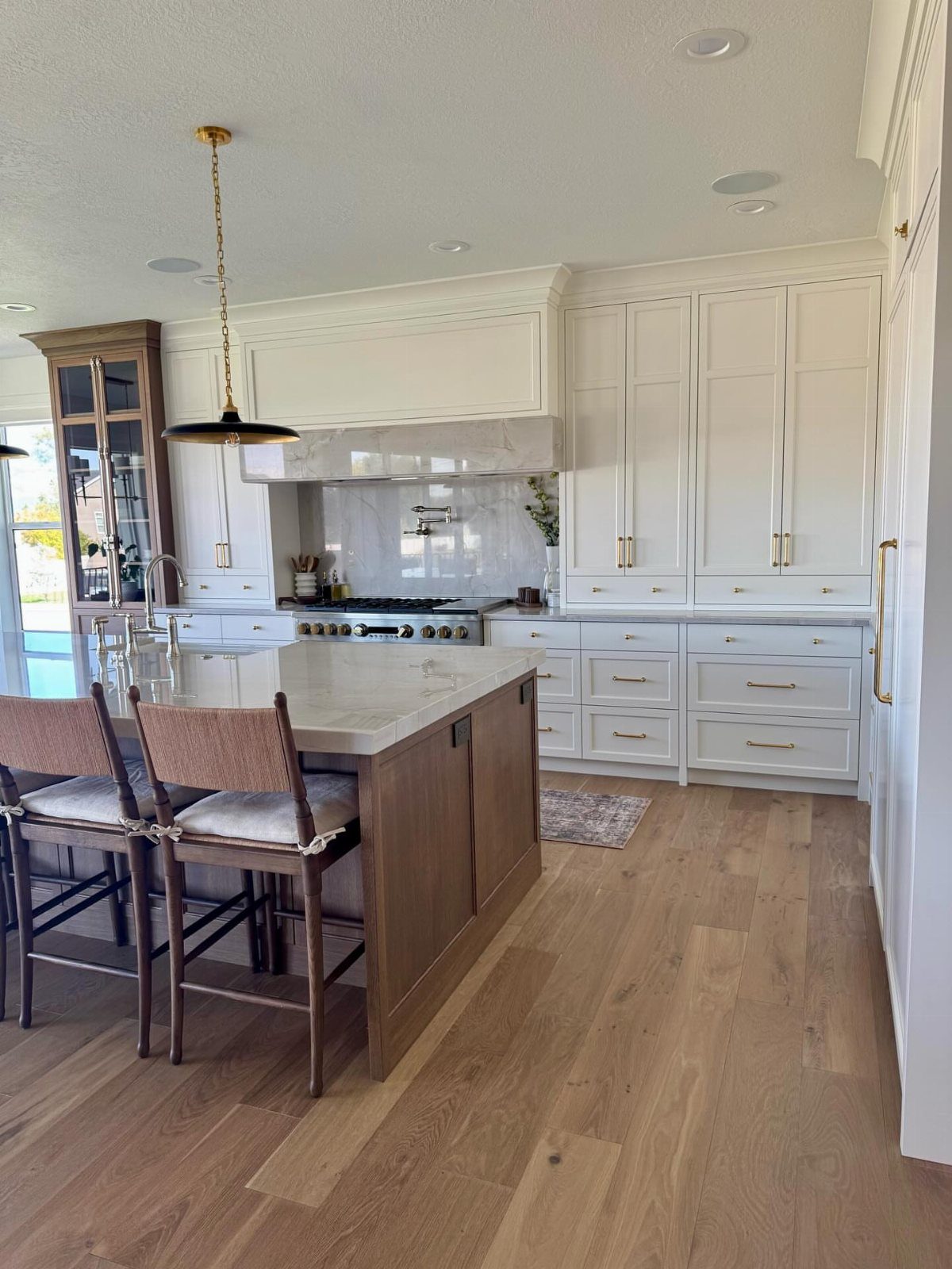 Light oak wood flooring in a bright modern kitchen with white cabinets and marble island.