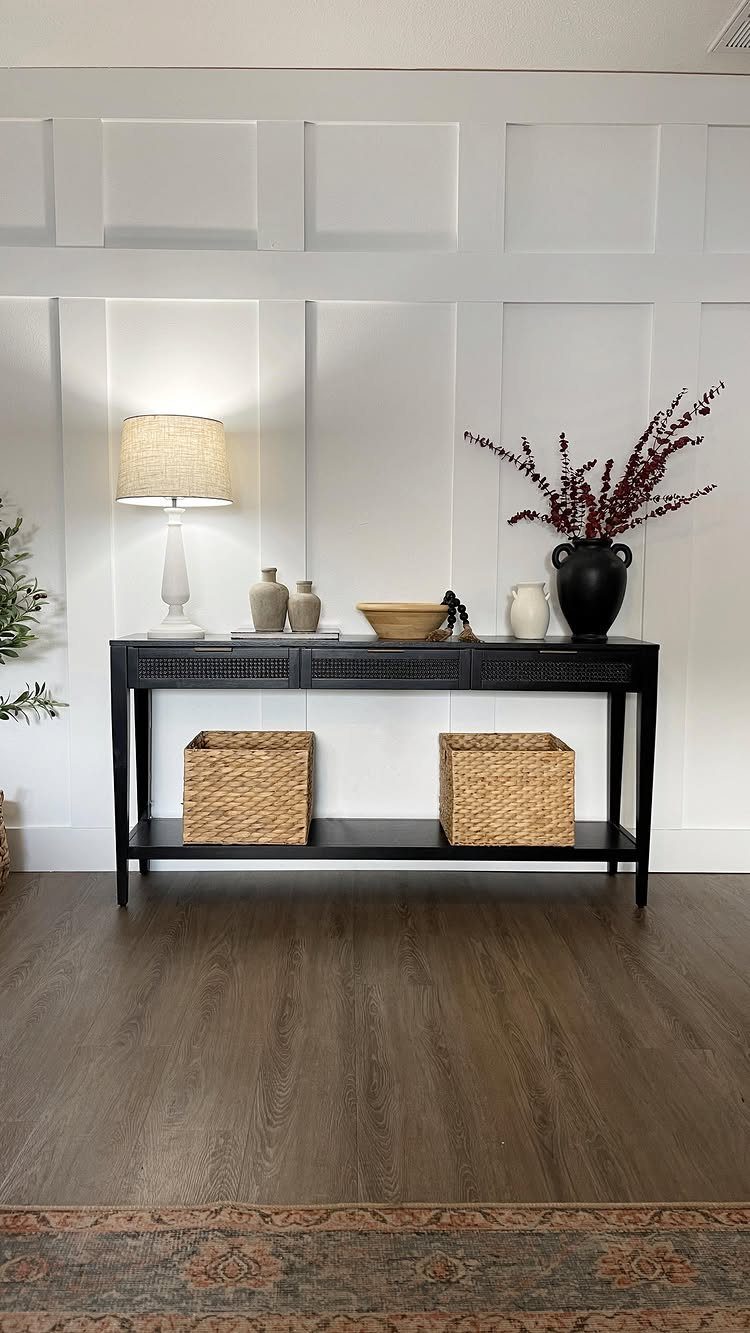 White paneled wainscotting accent wall behind a black console table with decor and wicker baskets.