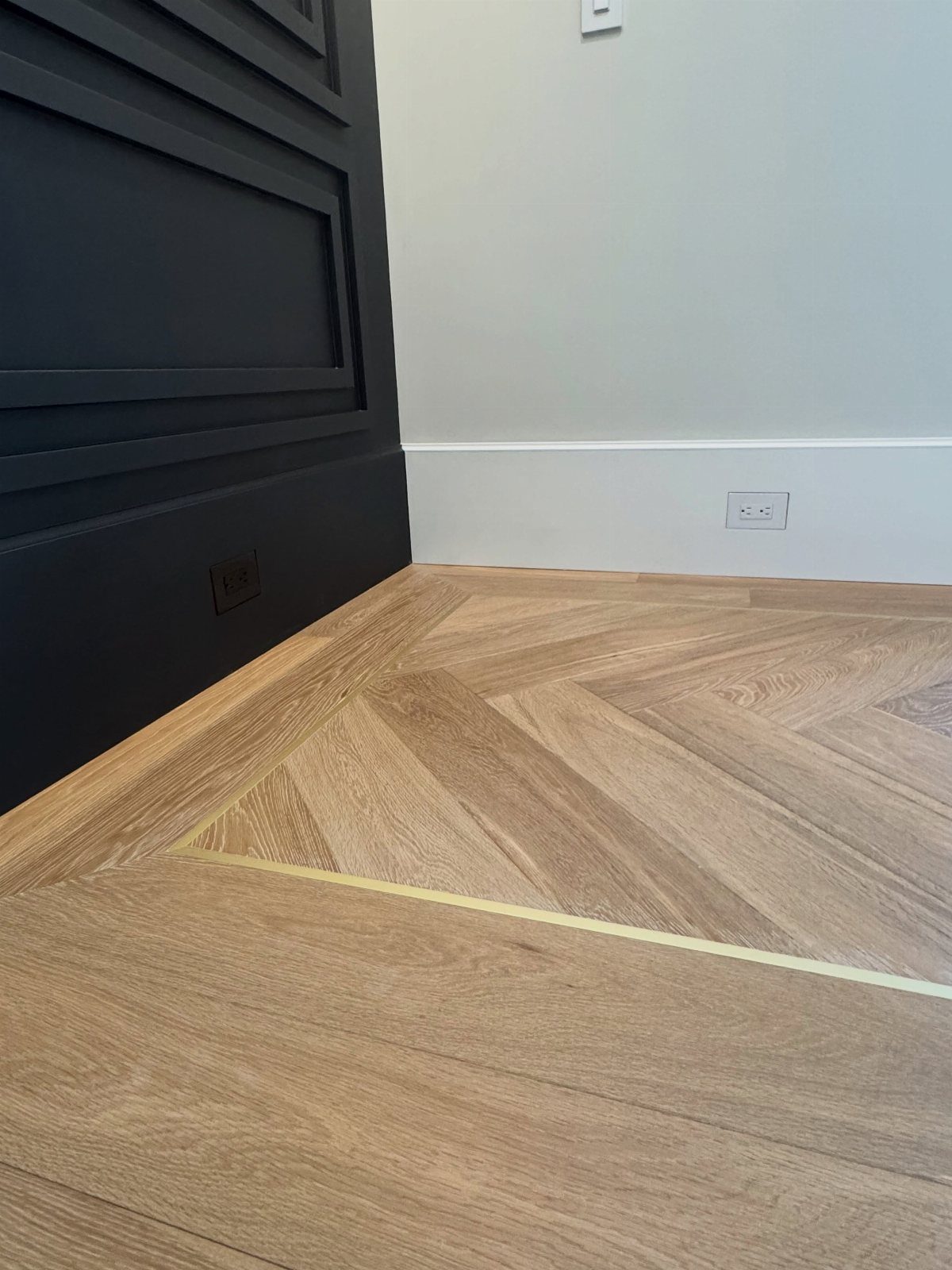 11 Luxury Living Room Flooring Ideas for 2026 9 Light brown wood flooring with a herringbone pattern and a gold metallic inlay strip.