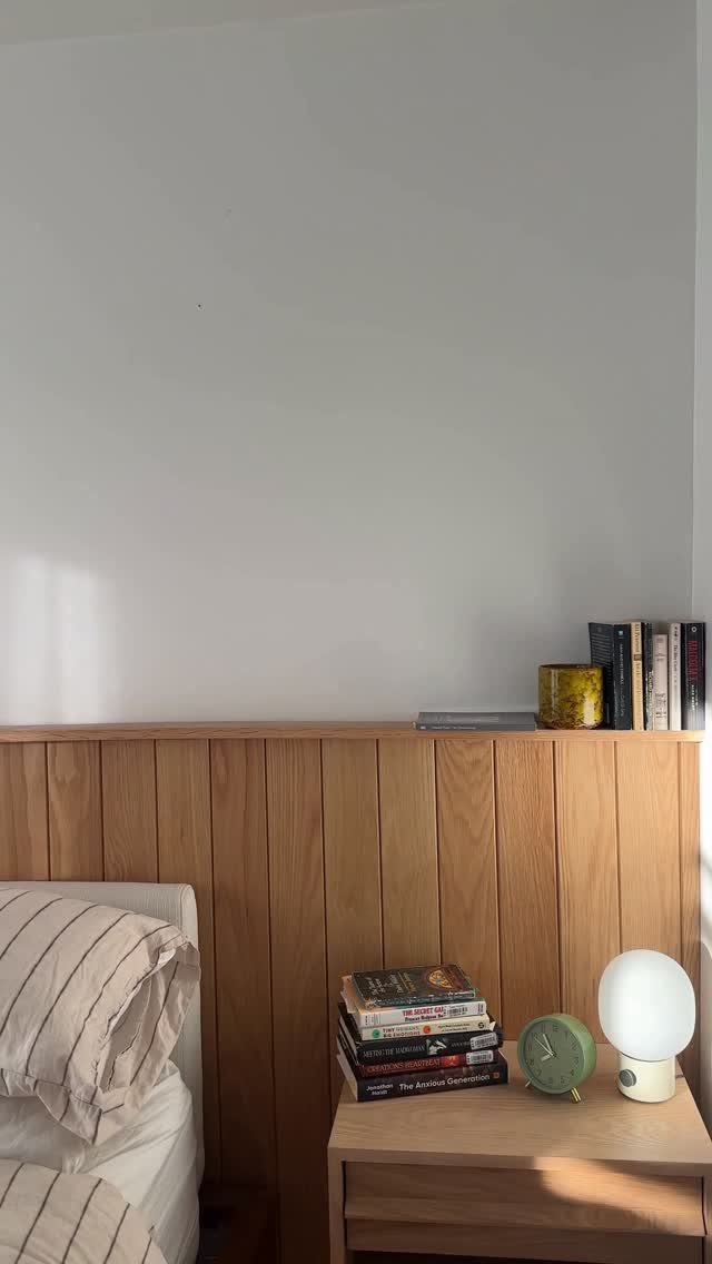 Wooden vertical slat paneling acting as an extended headboard against a white bedroom wall.