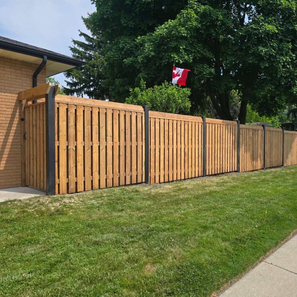 Vertical wooden fence panels installed between dark metal steel posts along a green lawn.